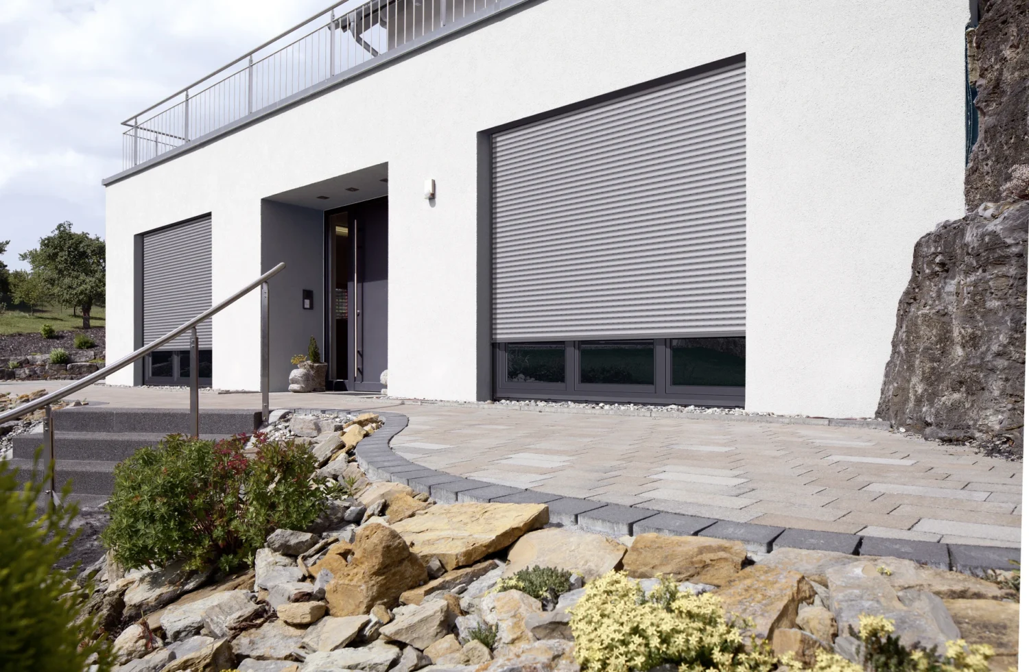 Moderne Hausfassade mit geschlossenen Rollläden und gepflegtem Steingarten